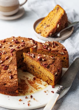 Triangular slices of Pumpkin Pecan Coffee Cake on a marble cake plate, one slice on a plate in the background with a cup of coffee.