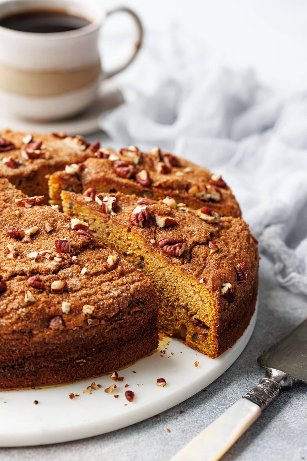 Slices of Pumpkin Pecan Coffee Cake on a marble cake plate with cup of coffee in the. background.