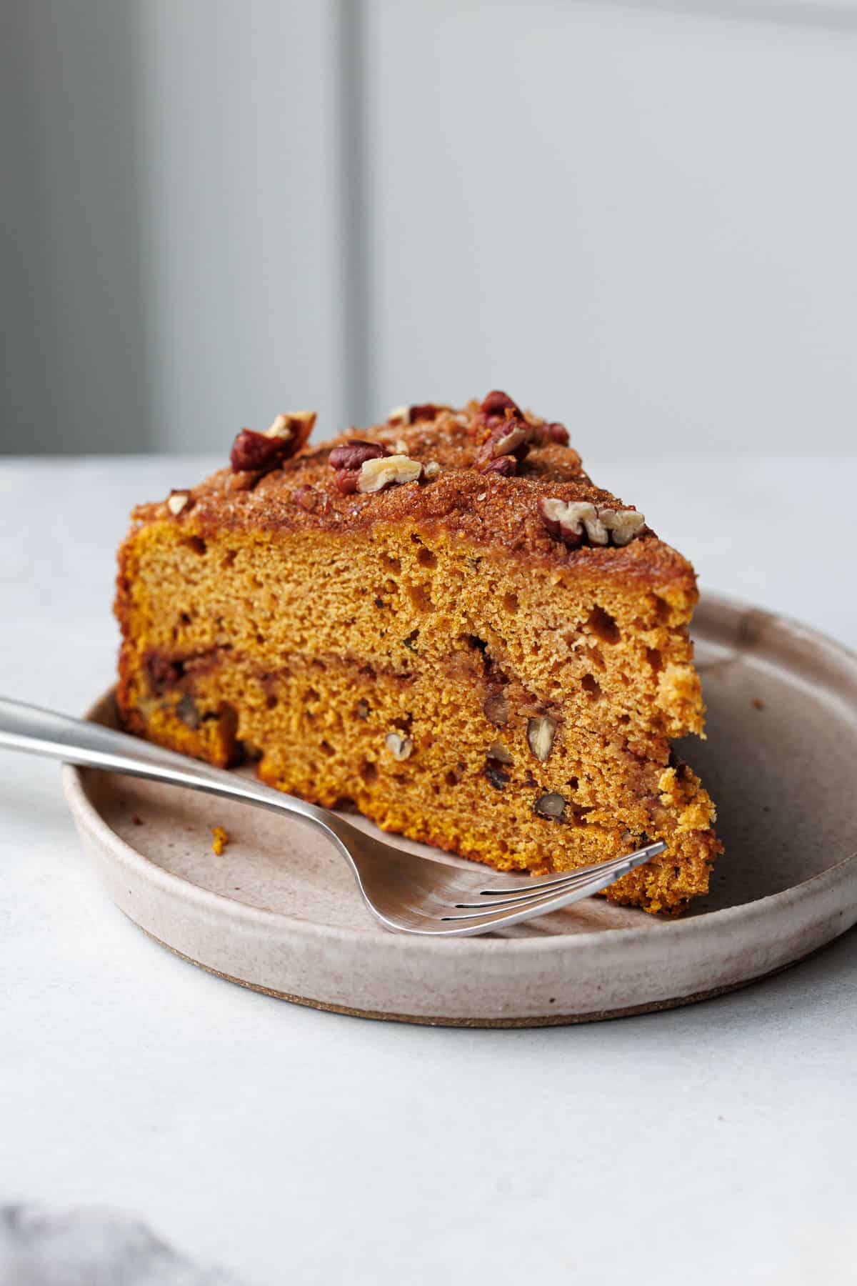 Closeup slice of Pumpkin Pecan Coffee Cake on a plate with fork, showing the moist crumb, cinnamon swirl, and crunchy topping.