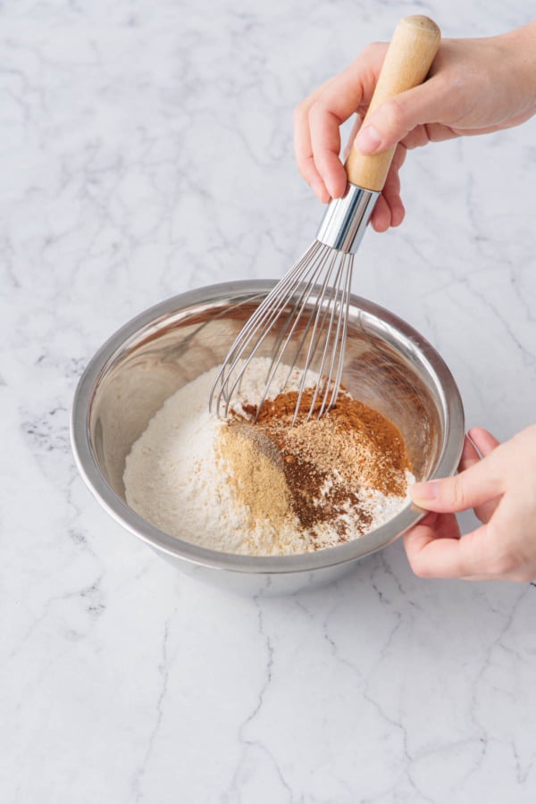 Whisking dry ingredients with pumpkin spices in a small metal mixing bowl.