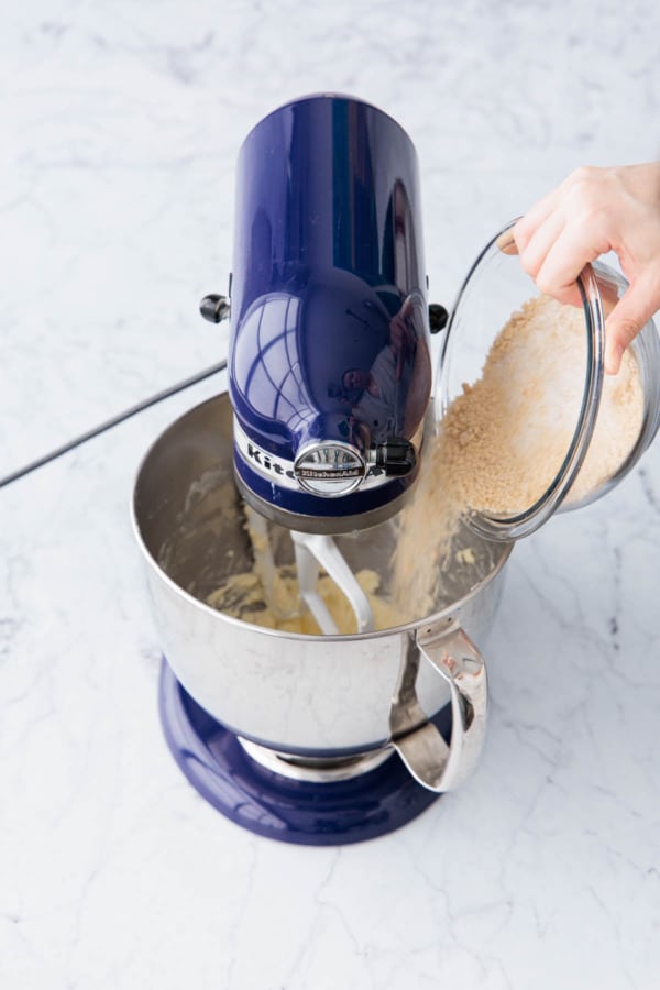 Pouring a mix of sugar and brown sugar into a mixing bowl with creamed butter.
