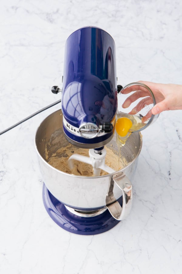 Adding one egg to mixing bowl with creamed butter and sugar.