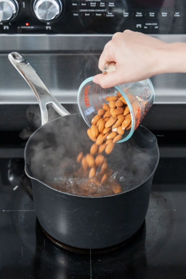 Dumping whole raw almonds into a saucepan with boiling water to blanch.