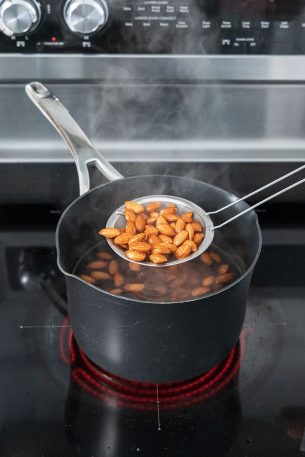 Draining blanched almonds from boiling water with a fine mesh skimmer.