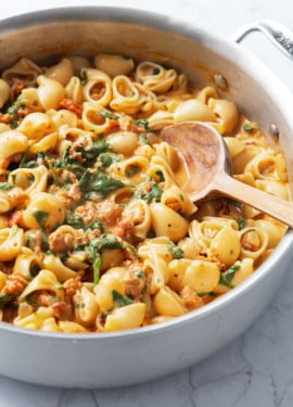 Closeup of stainless saucepan with Creamy Sundried Tomato and Italian Sausage Pasta and a wooden spoon.