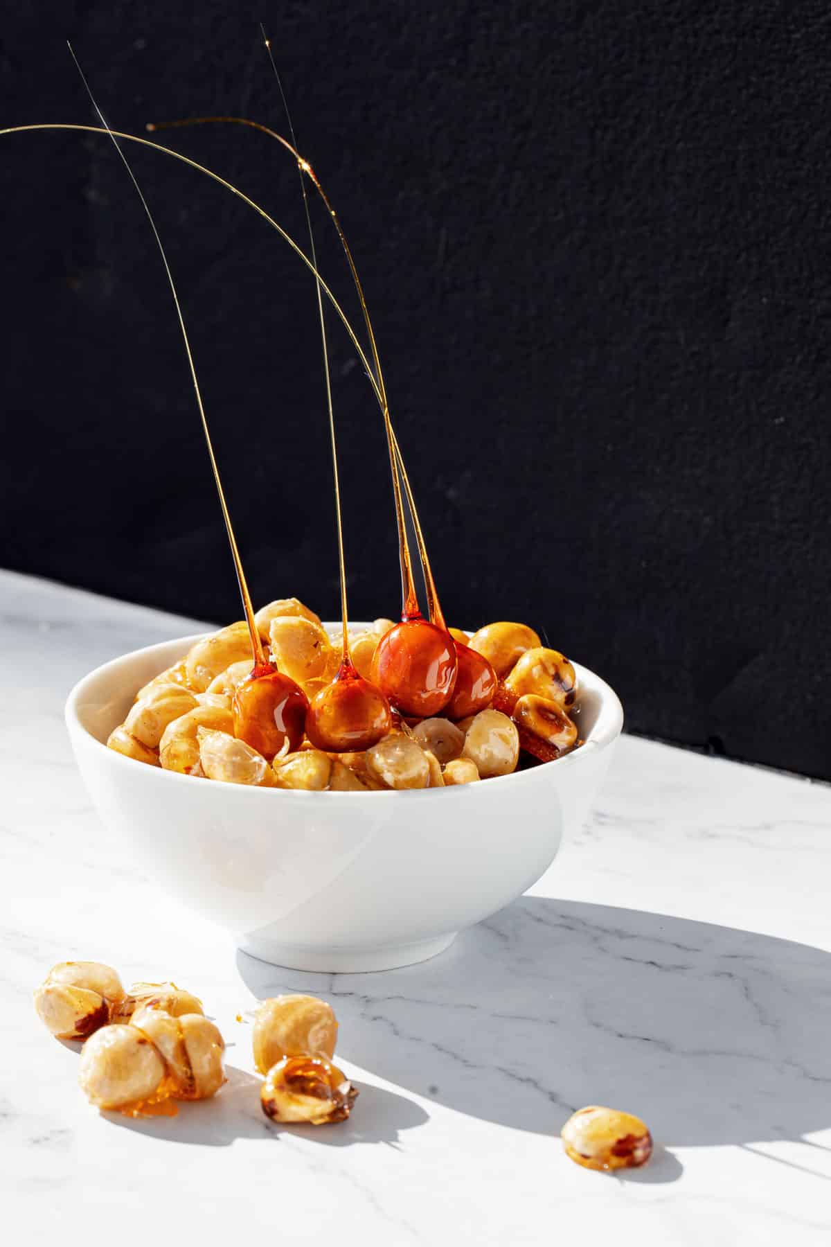 White bowl of candied hazelnuts and hazelnut spikes with a dramatic black and white background.
