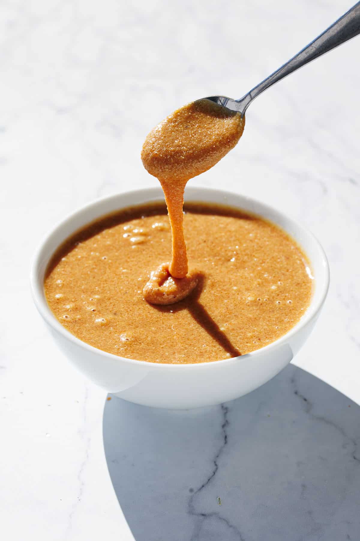 Bowl of homemade hazelnut praline with a spoon lifting some out to show the consistency.