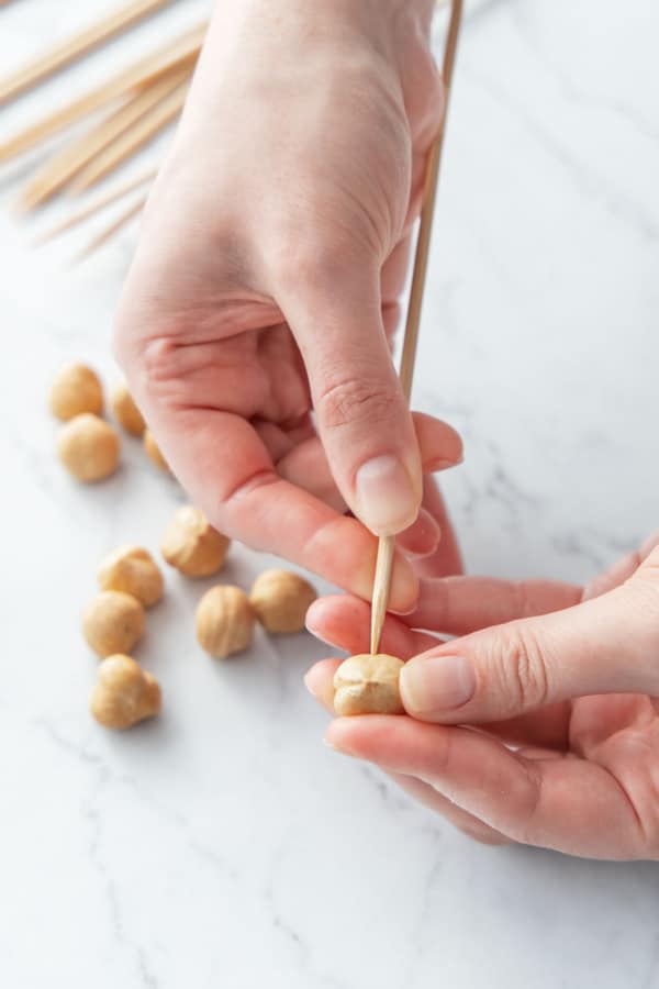 Inserting a wooden skewer into the side of a peeled whole hazelnut.
