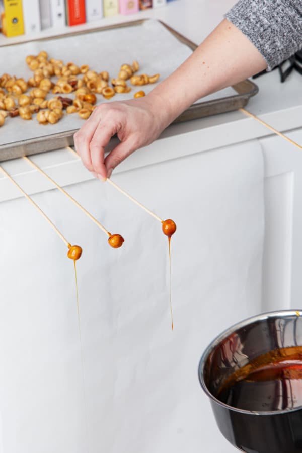 Sliding skewer underneath a baking sheet overhanging the countertop to allow the caramel to drip.