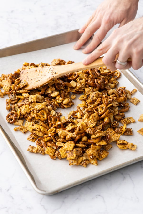 Spreading snack mix evenly over the full surface of the baking sheet.