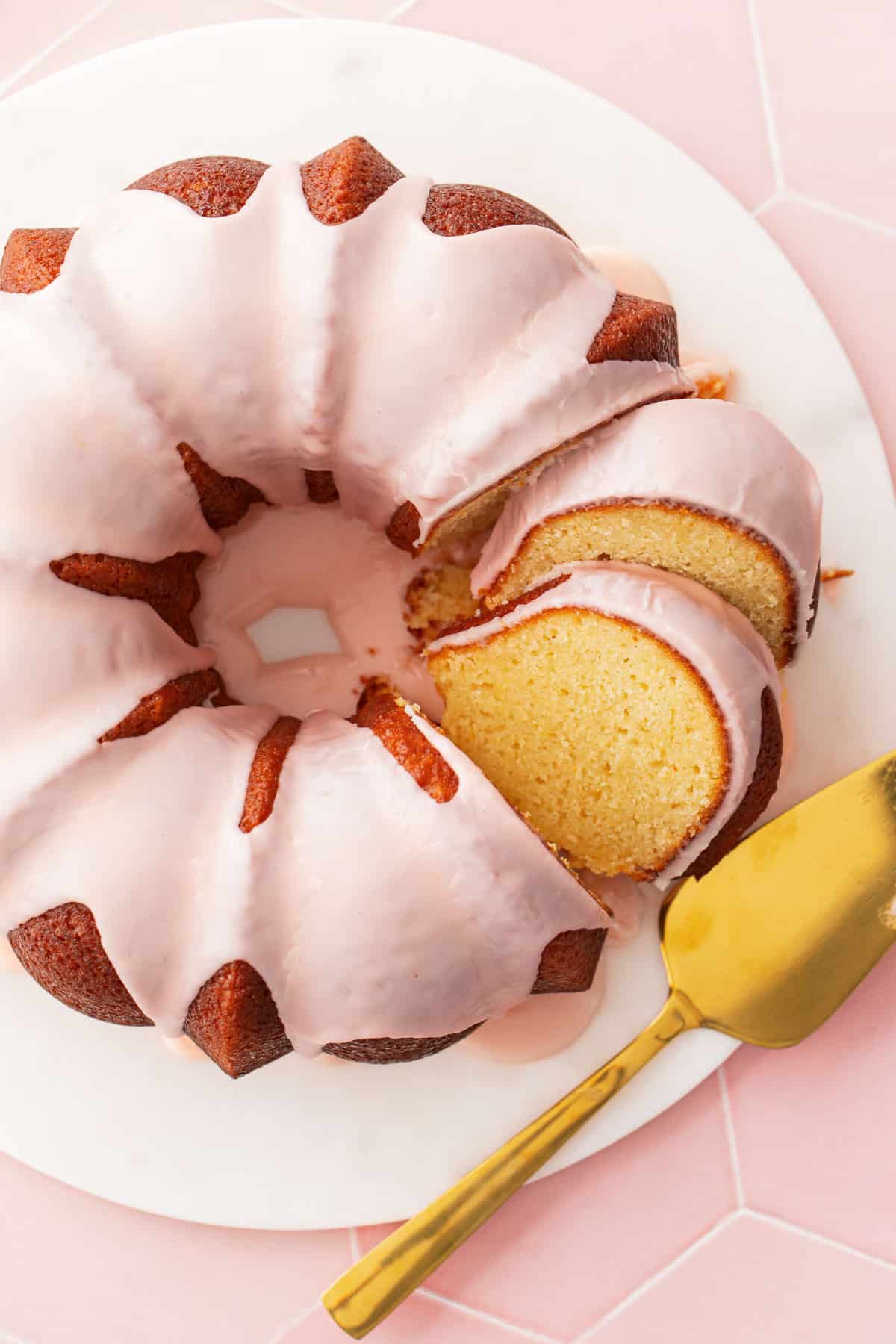 Overhead, Grapefruit Olive Oil Bundt Cake on a marble cake plate with a few slices cut and leaning against each other to show the texture, with a gold cake server on the side.