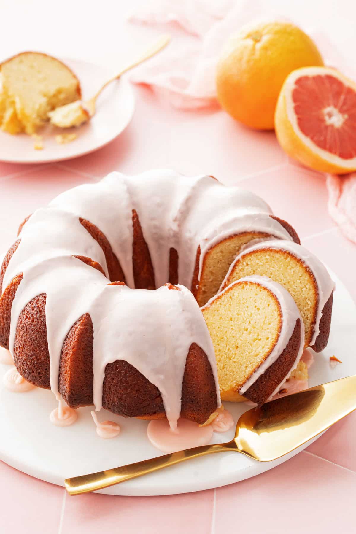 Grapefruit Olive Oil Bundt Cake with two cut slices leaning against each other, on a white cake plate and cut grapefruit and a slice of cake in the background.