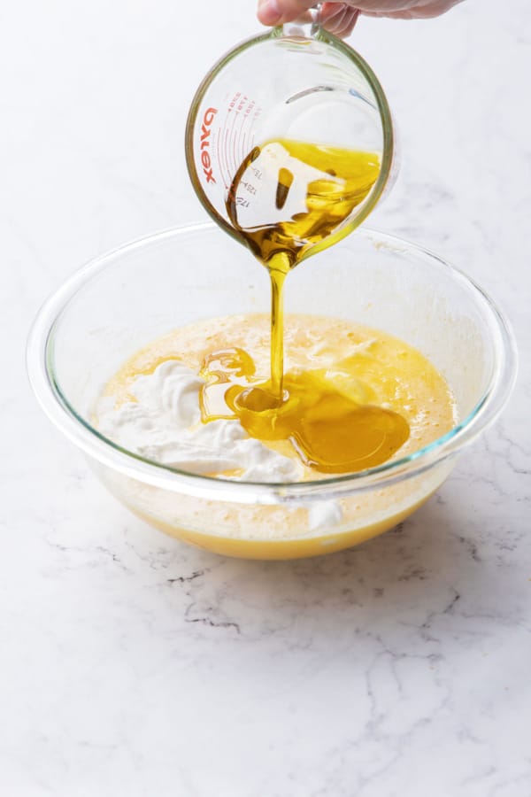 Adding olive oil to mixing bowl with egg and sugar mixture.