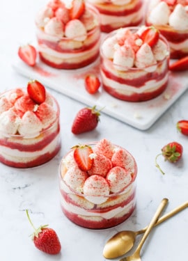 Strawberry Elderflower Tiramisu in individual clear ramekins, on a white marble background with two gold spoons and strawberries.