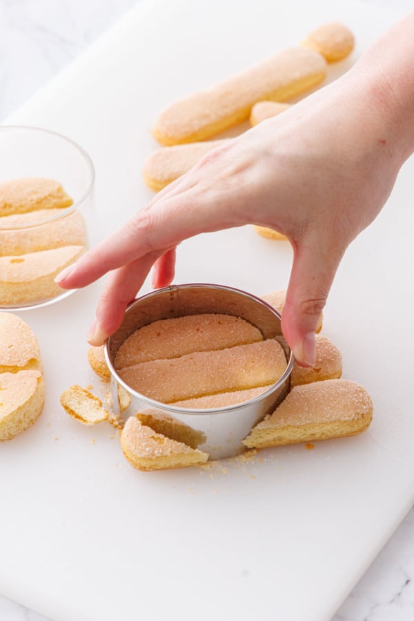 Cutting ladyfinger cookies into rounds with a circle cookie cutter.