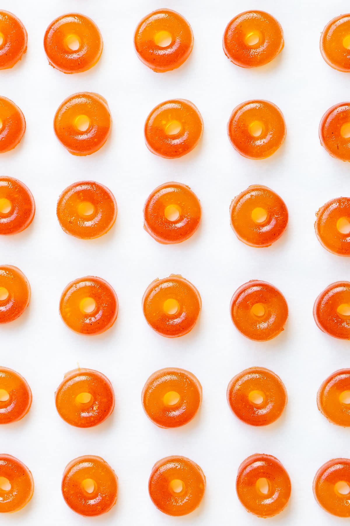 Overhead, even rows of Homemade Gummy Peach Rings lined up on a piece of white parchment paper.