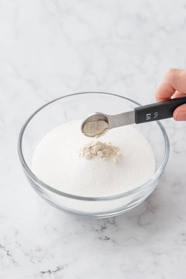 Measuring guar gum into a small bowl filled with granulated sugar.