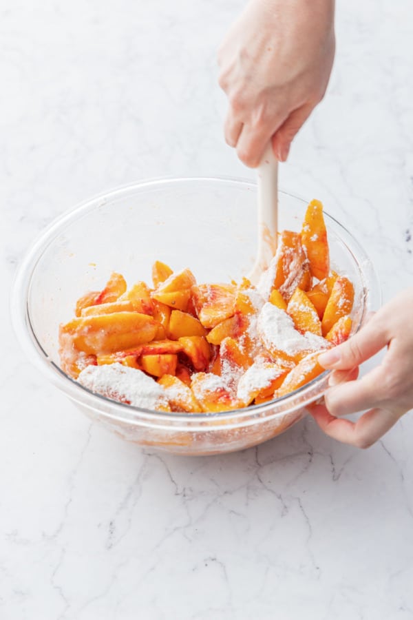 Stirring peach pie filling with a silicone spatula until evenly coated with cornstarch/sugar mixture.