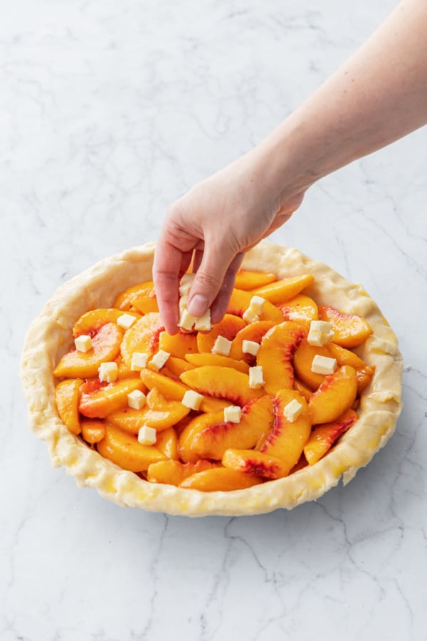 Dropping small cubes of butter evenly over the top of the peaches.