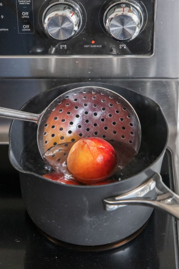 Submerging fresh peach into boiling water to help with the peeling.