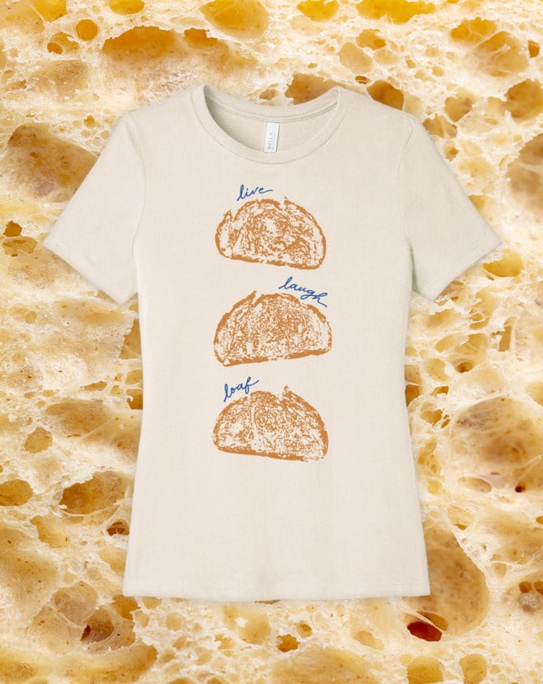 Image of a natural tshirt reading "Live Laugh Loaf" on a background of closeup bread texture.