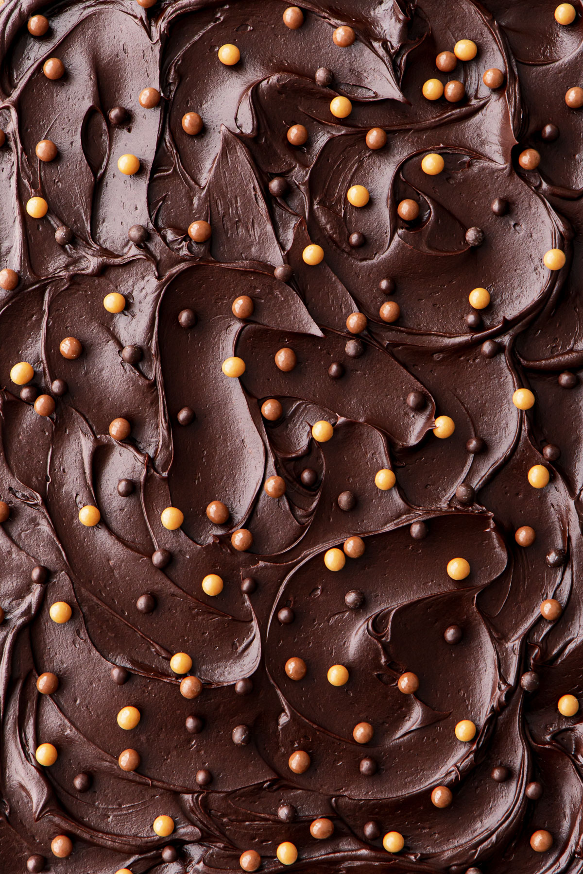 Overhead, closeup of the frosted top with swooping, shiny chocolate swirls and dotted with chocolate crisp pearls.