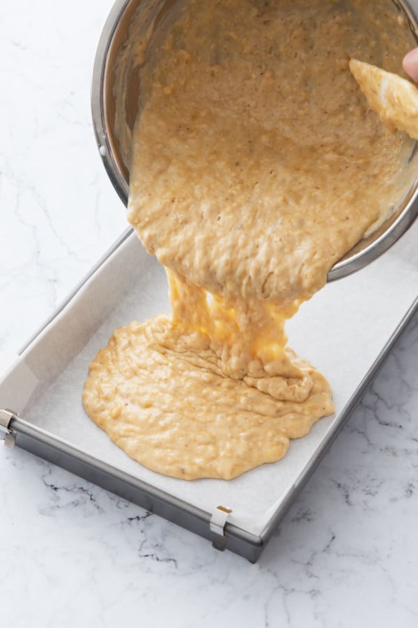 Pouring banana cake batter into a parchment lined baking pan.