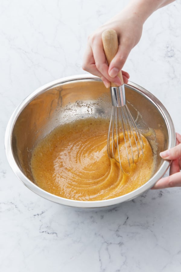 Whisking eggs into butter and sugar mixture until smooth.