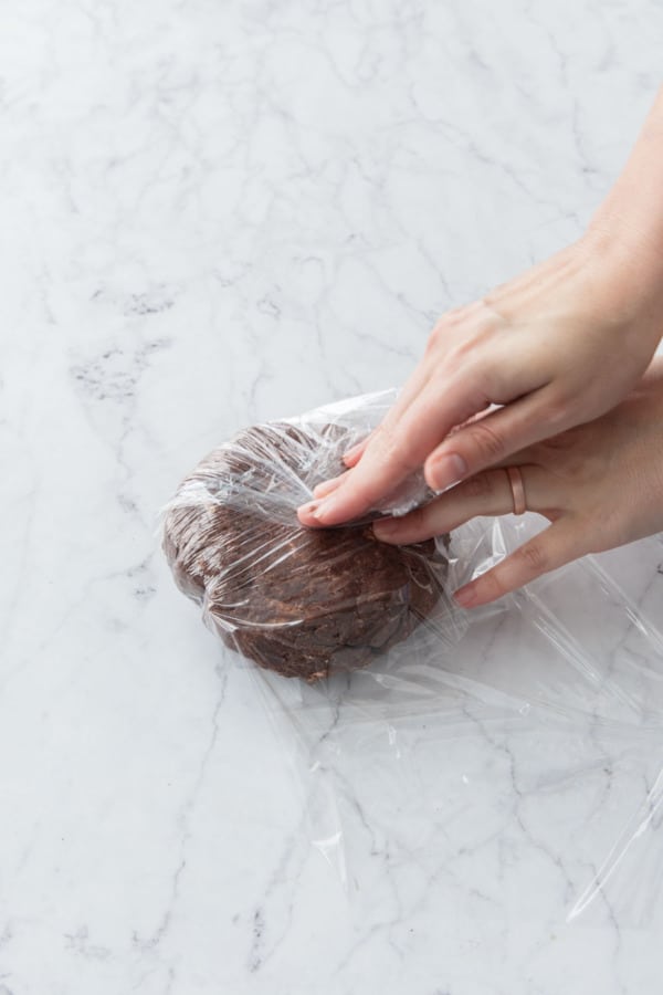 Wrapping chocolate pie dough tightly in plastic wrap.