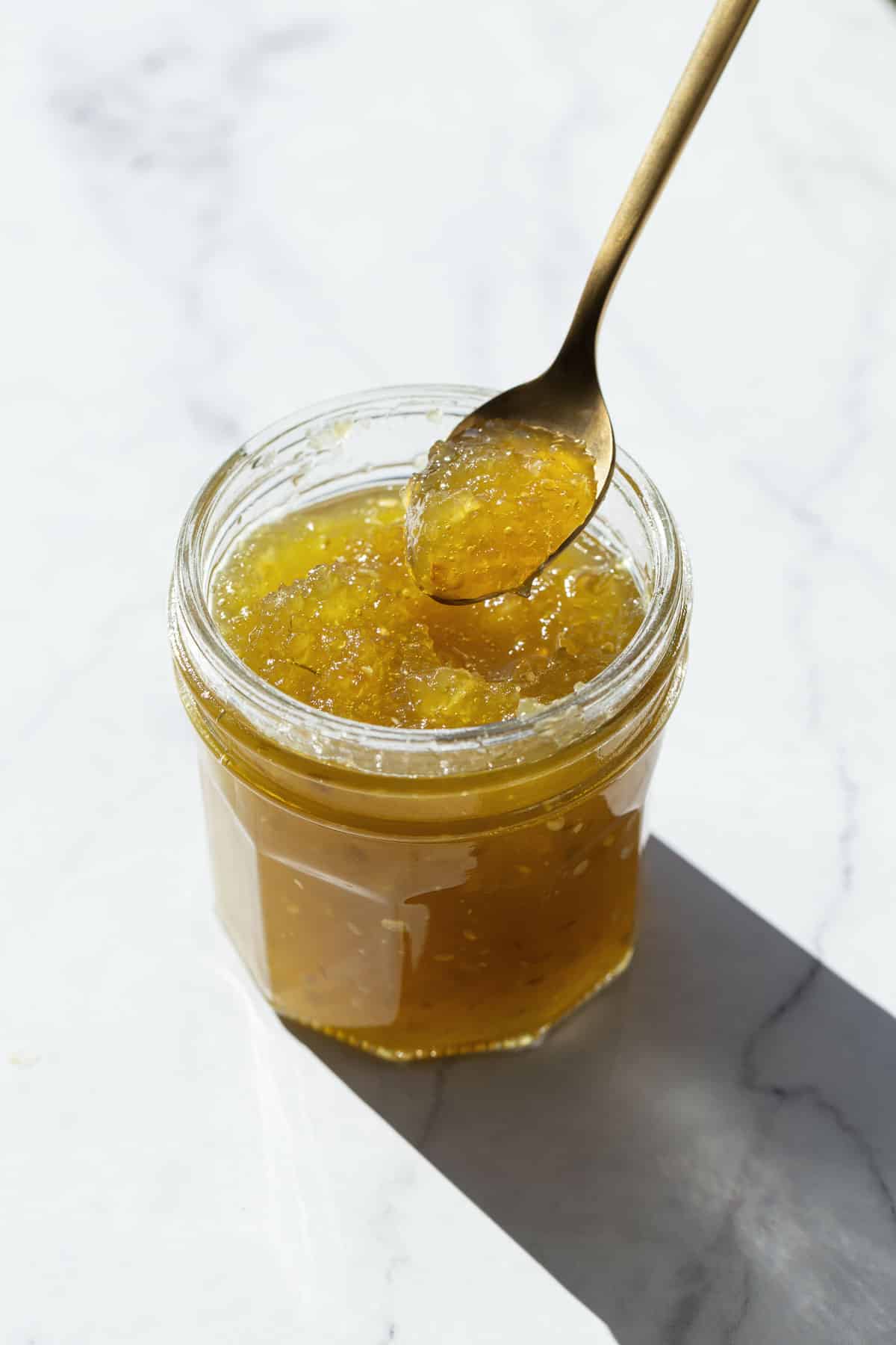 Open jar of Green Tomato Jam with a spoonful lifting out to show the color and texture.
