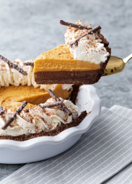 Lifting a slice of Black Bottom Pumpkin Cream Pie out of the pie plate, showing the distinct layers of chocolate ganache and pumpkin cream.