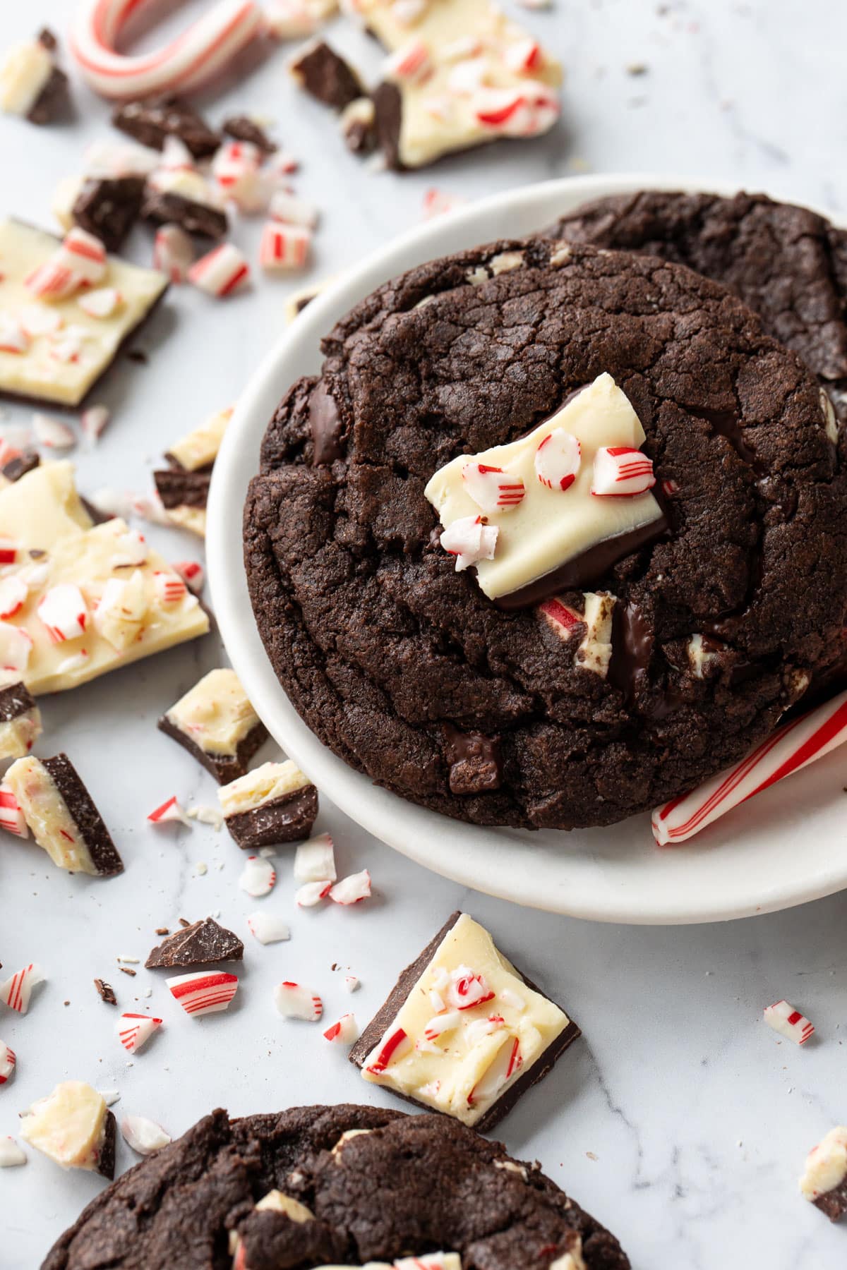 Two Chocolate Peppermint Bark Cookies on a small cookie plate, with bits of broken peppermint bark and candy canes scattered around.