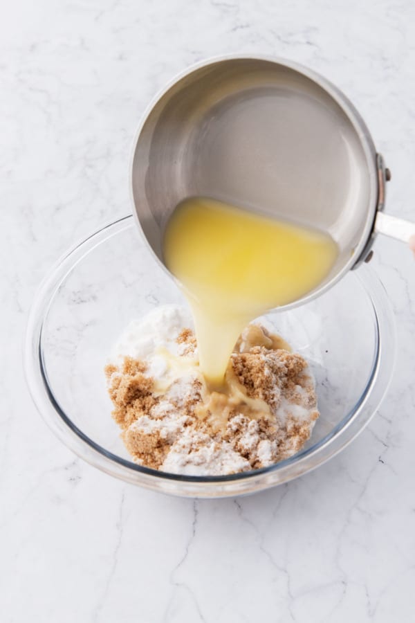 Pouring melted butter into a mixing bowl with white and brown sugars.