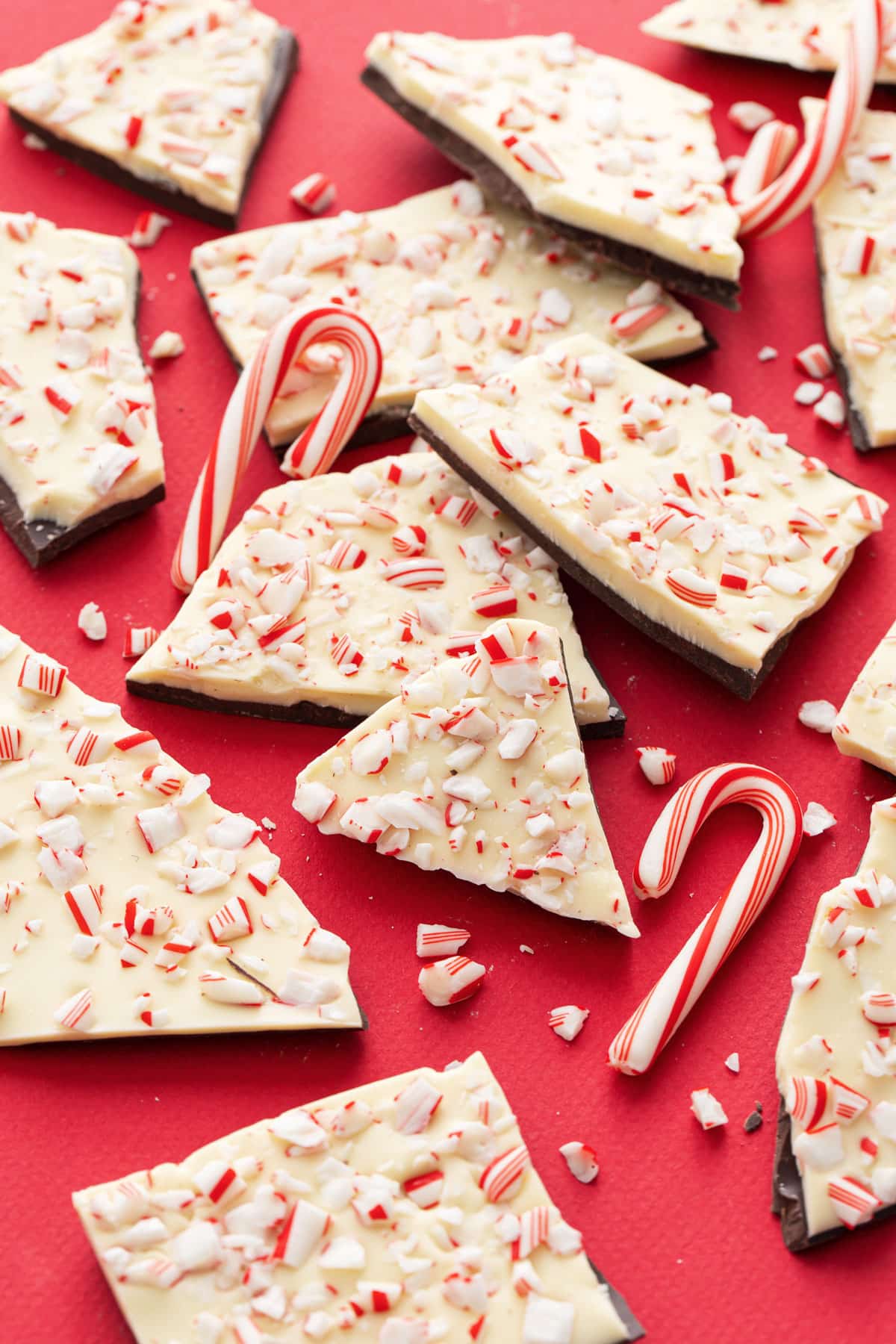 Rough broken pieces of homemade peppermint bark scattered on a red background with bits of crushed candy canes scattered around.