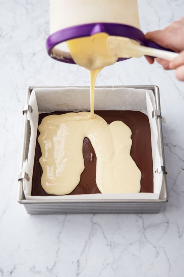 Pouring white chocolate onto partially-set dark chocolate layer in the square baking pan.