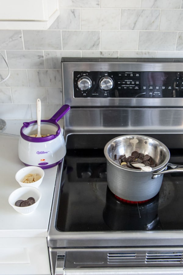 Stovetop with a double boiler melting dark chocolate, and a chocolate pot to melt the white chocolate.