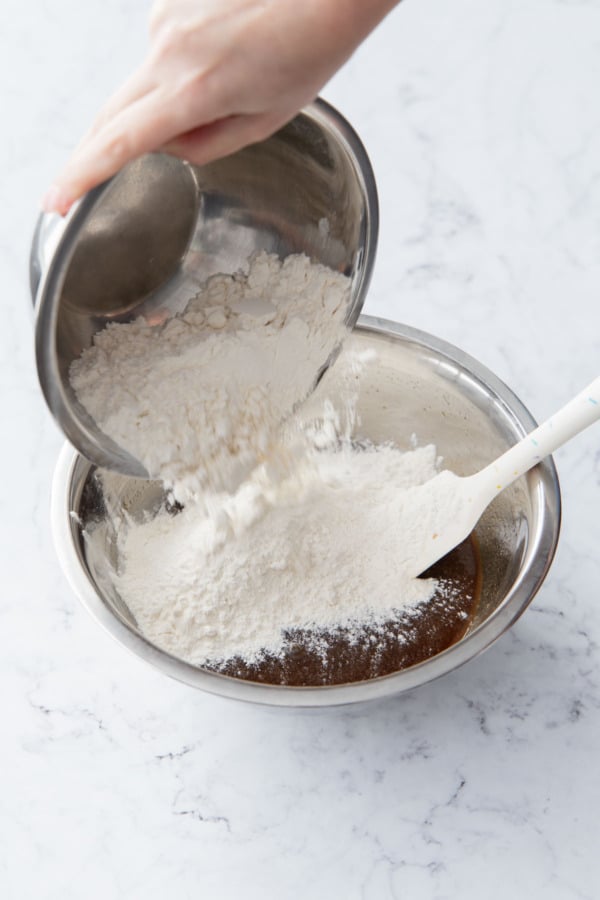Adding dry ingredients to the mixing bowl with the wet ingredients.