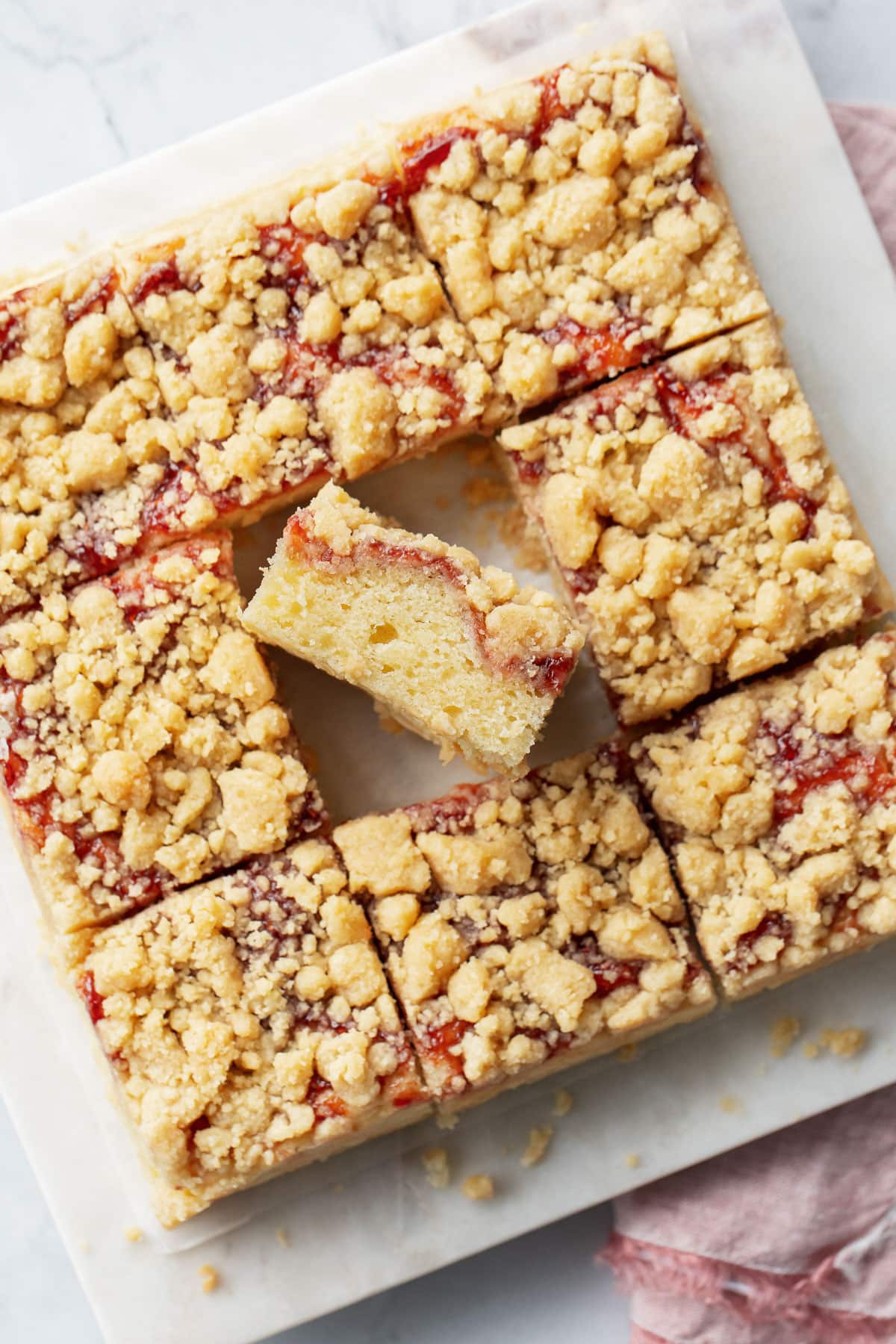 Overhead view of Jammy Sour Cream Crumb Cake cut into squares, one set on its side to show the layers of cake, jam, and crumb.