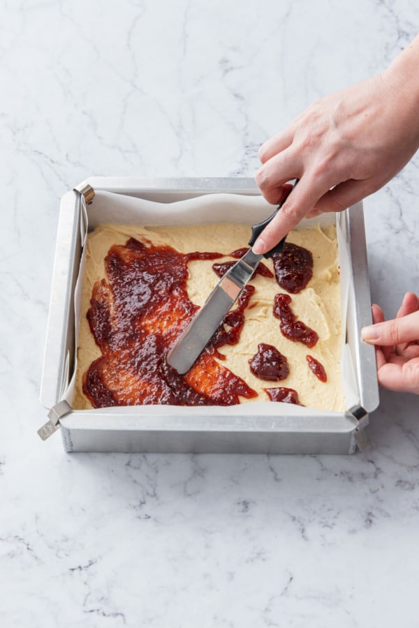Spreading jam into an even layer on top of cake batter with an offset spatula.