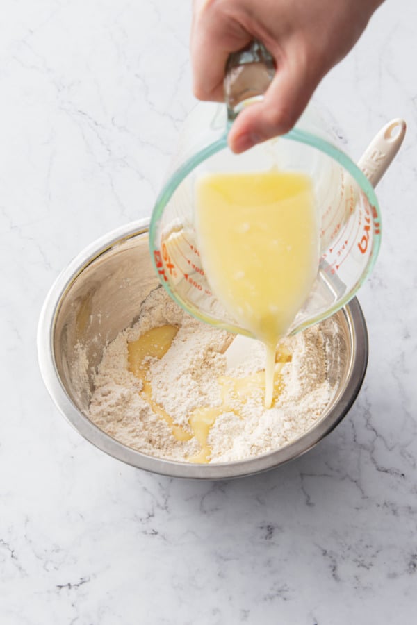 Pouring melted butter into a mixing bowl with dry ingredients.