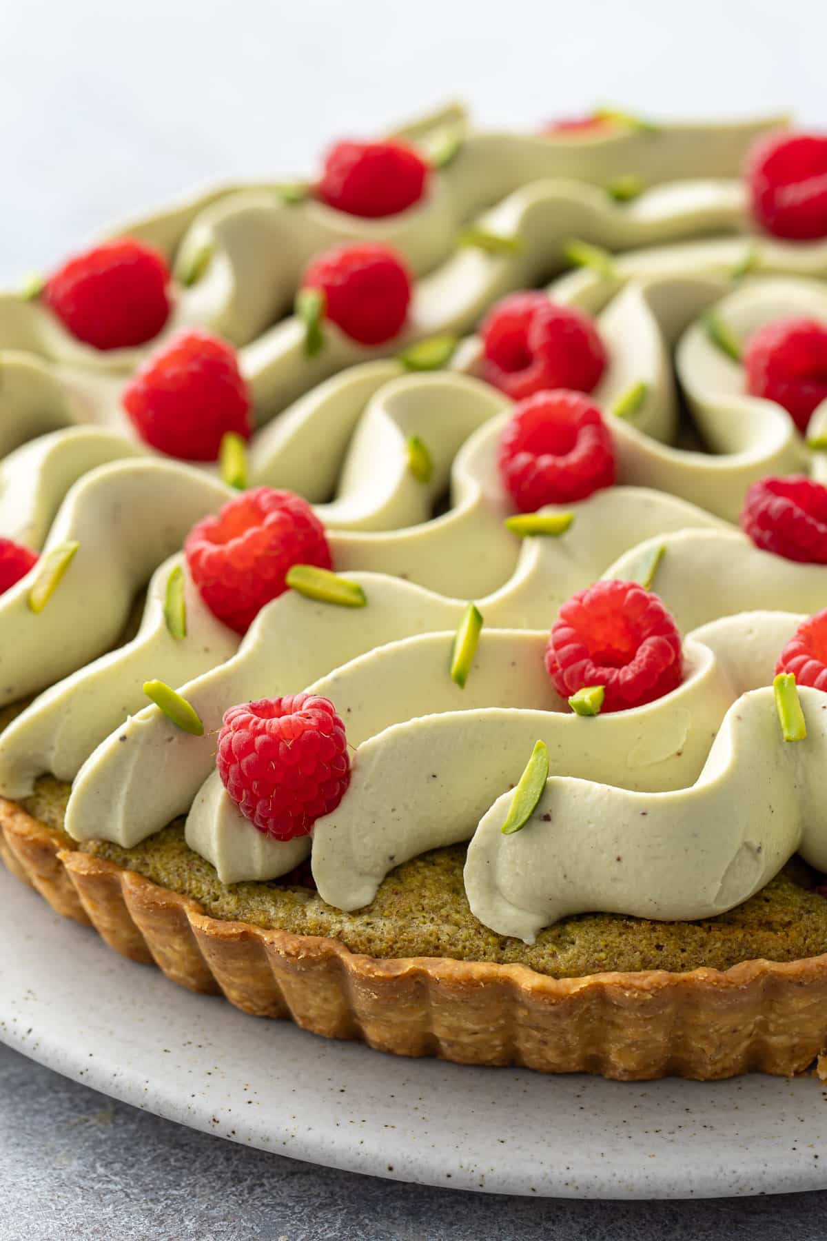 Whipped pistachio ganache piped in flowing, organic waves on top of a pistachio frangipane tart, garnished with fresh raspberries and slivered pistachios.