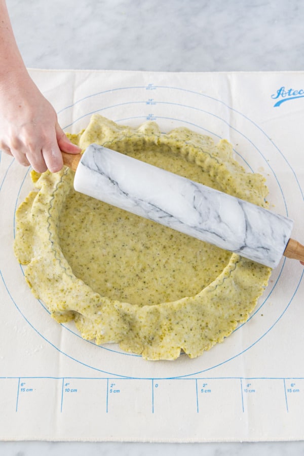 Rolling pin being used to trim the excess dough off the tart pan.