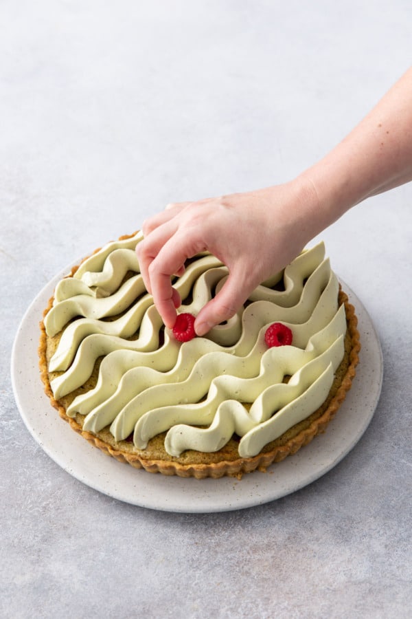 Placing a few fresh raspberries on top of the tart for decoration.