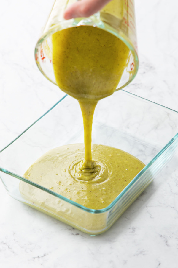 Pouring pistachio ganache into a shallow glass baking dish to cool.