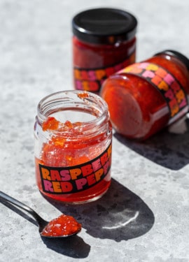 Three jars of Raspberry Red Pepper Jelly, one open and a spoonful sitting in the foreground to show the texture of the jelly.