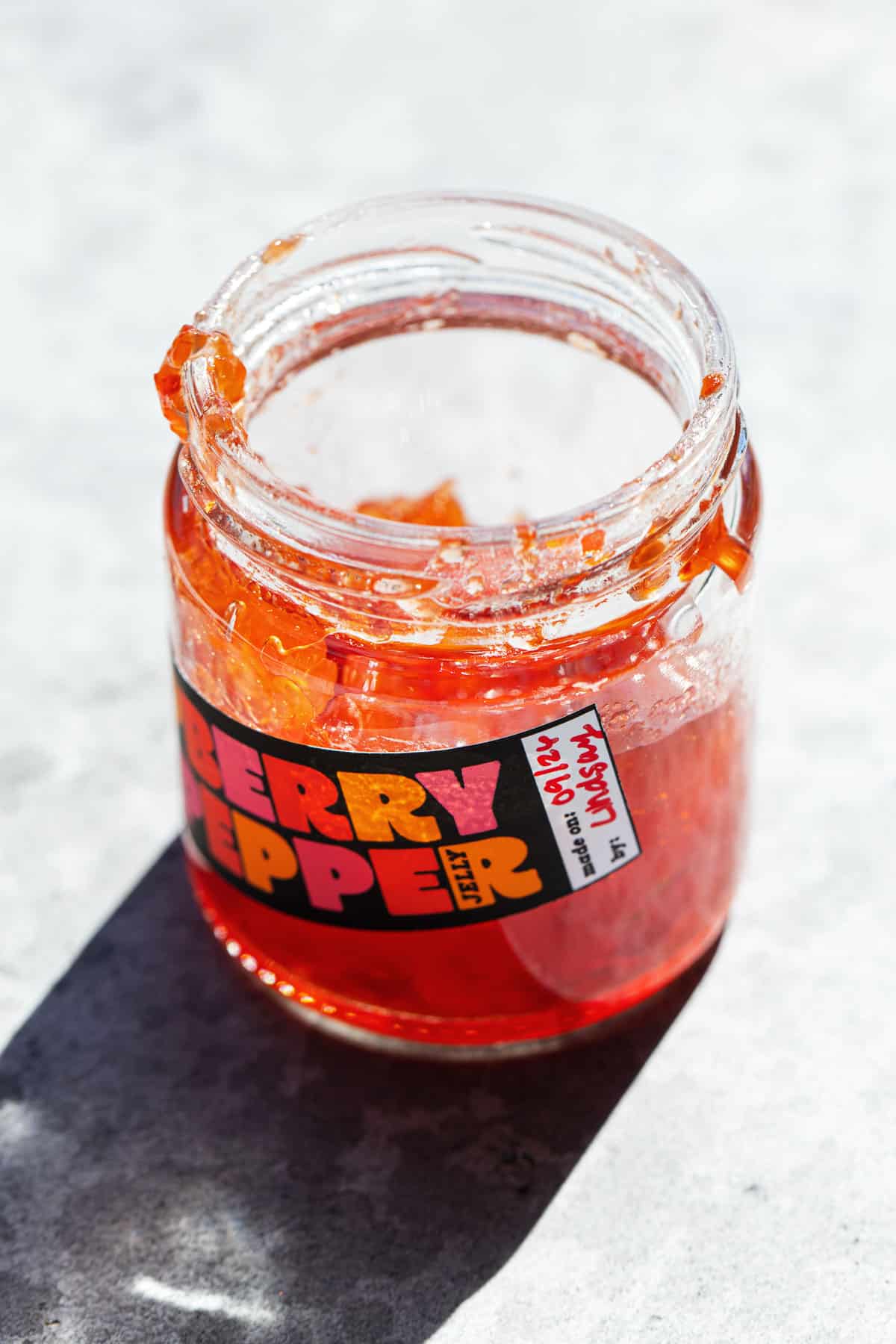 Backlit jar of Raspberry Red Pepper Jelly, the light making the jelly look like stained glass, with a custom printable label.