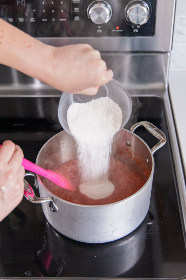 Adding pectin whisked with 1/2 cup of the sugar to saucepan with softened peppers.